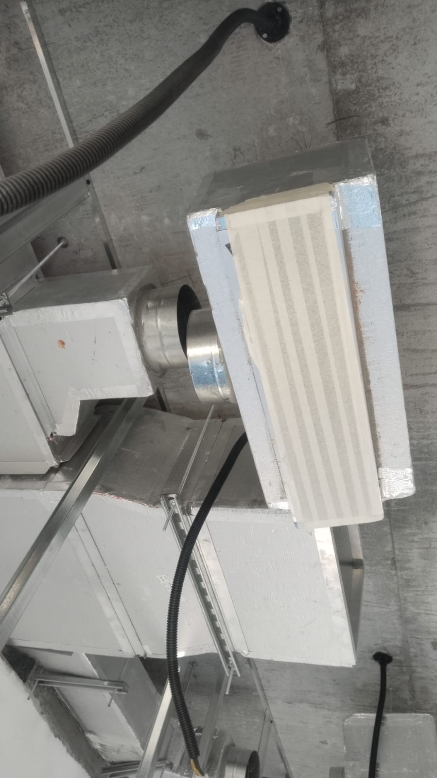 Round duct connection beside insulated rectangular ductwork above ceiling framing.